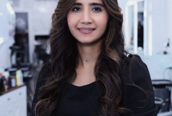 Smiling woman with long, dark wavy hair wearing a black top inside Davida Salon in NYC.