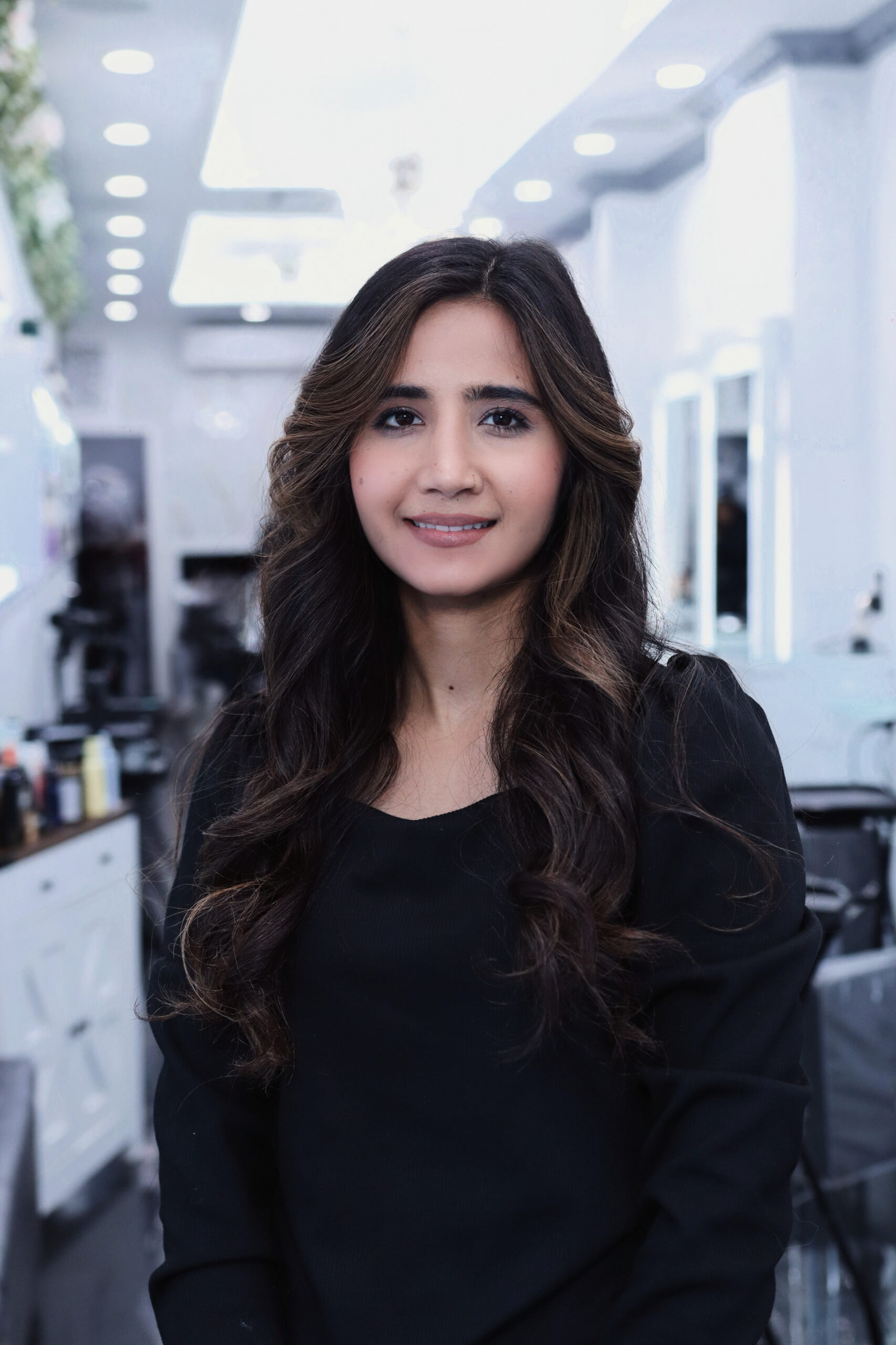 Smiling woman with long, dark wavy hair wearing a black top inside Davida Salon in NYC.