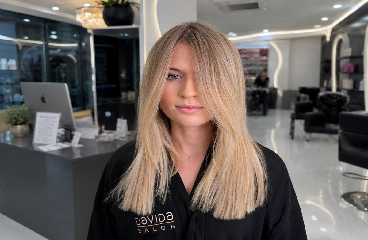 A woman showcasing smooth, sleek blonde hair following a professional keratin treatment at Davida Salon.